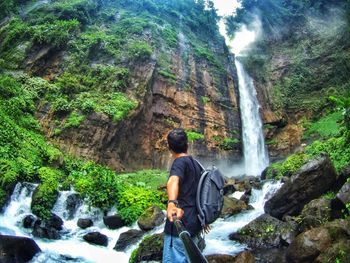Man holding with monopod standing in front of majestic waterfall