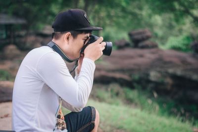 Side view of young man photographing with camera in forest