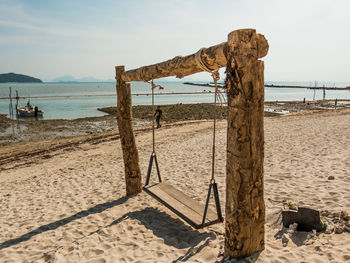 Wooden swing on beach against sky