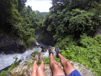 Low section of couple relaxing on cliff by river in forest