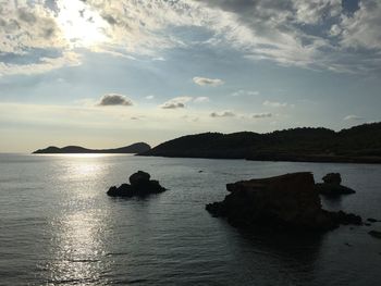 Silhouette rocks on sea against sky during sunset