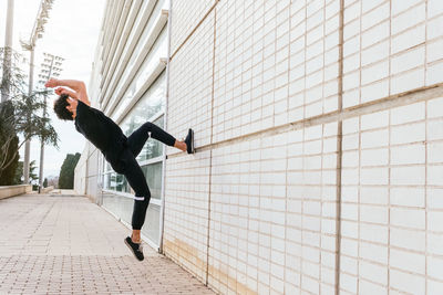 Side view of full length faceless man in black outfit performing acrobatic parkour stunt while jumping above ground near building