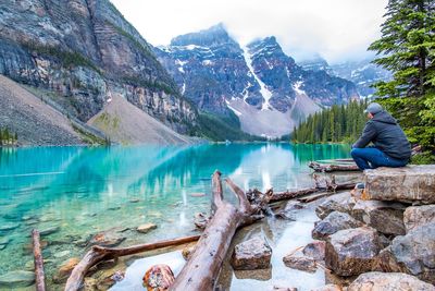 Man sitting on rock by river against mountains