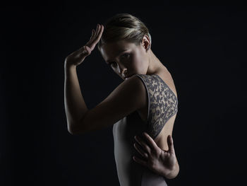 Woman looking away while standing against black background