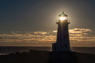 Lighthouse by sea against sky during sunset