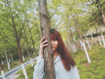 Portrait of young woman standing behind tree