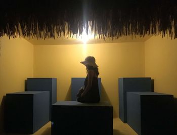 Side view of man sitting on table against illuminated wall