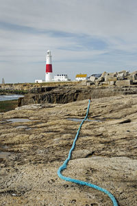 Lighthouse on rock by building against sky