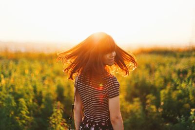 Rear view of young woman with tousled hair standing on field during sunset