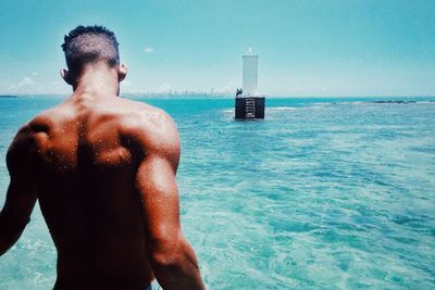 Rear view of shirtless man standing in sea against sky