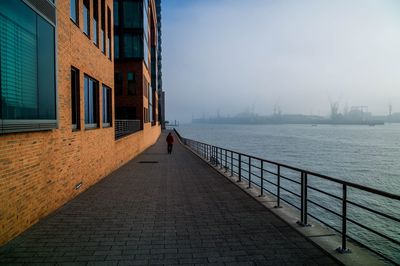 Footpath by sea against sky in city