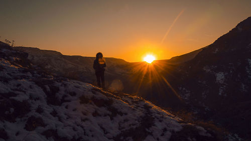 Silhouette person walking on snow covered landscape during sunset