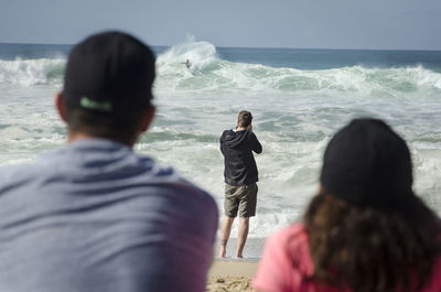 Rear view of people looking at surfer against clear sky