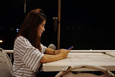 Side view young woman using phone while sitting on restaurant table