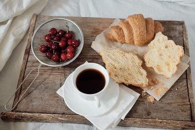 Tasty breakfast with fresh croissant, coffee, cherries on a wooden tray. hearty croissant 