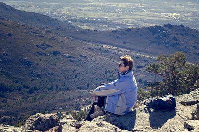 Side view full length of woman sitting on mountain at navacerrada