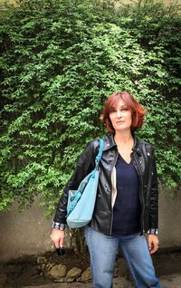 Portrait of woman in leather jacket standing against plants