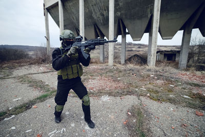 Army soldier aiming while standing against built structure