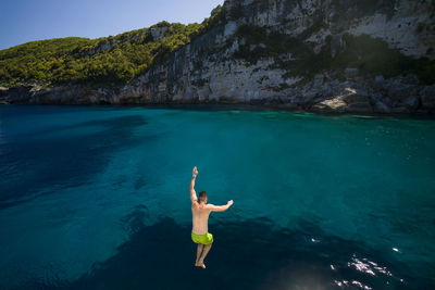 Rear view of shirtless man jumping in sea
