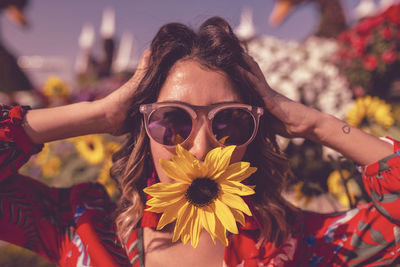 Portrait of woman wearing sunglasses on red flowering plant