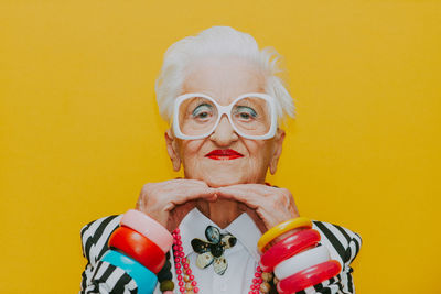 Portrait of smiling senior woman wearing eyeglasses against yellow background