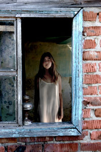 Portrait of a sad girl in the window of the old house