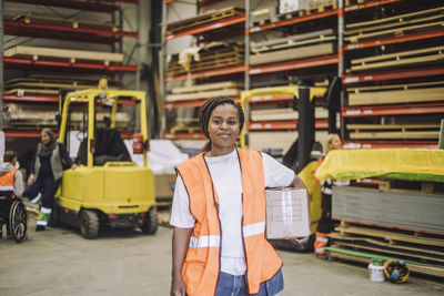 Portrait of smiling carpenter carrying cardboard box in warehouse