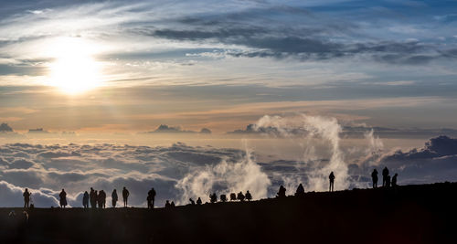 Silhouette people standing on mountain against cloudy sky during sunset