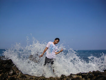 Waves splashing on man standing at beach against sky