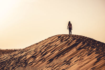 Woman walking on sand dune against clear sky during sunset