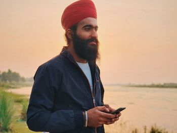 Young man using smart phone against sky during sunset