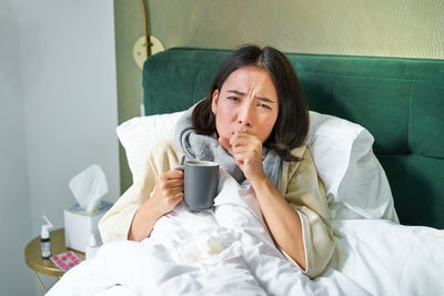 Young woman using mobile phone while sitting on bed at home