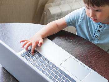 Curious toddler boy explores the laptop and presses buttons on computer keyboard.