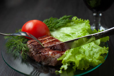 Delicious slice of beef steak on dish with vegetables and glass of red wine