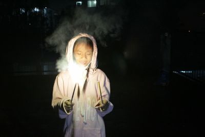 Girl wearing hooded shirt playing with sparklers at night