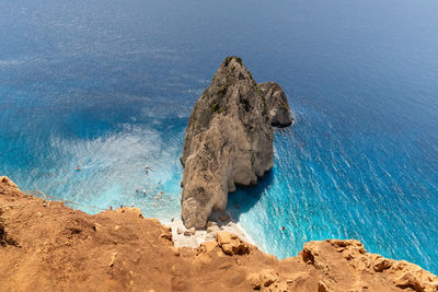 Beautiful view of a lonely cliff with a rocky beach and floating boats in the blue sea 