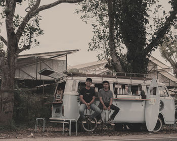 People sitting on sidewalk against trees