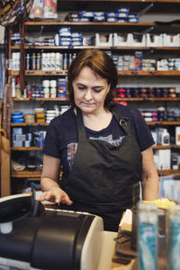 Woman using cash register in shoe repair shop