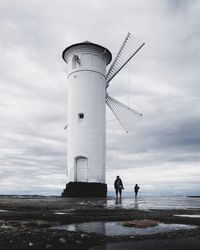 Low angle view of people standing by lighthouse against sky