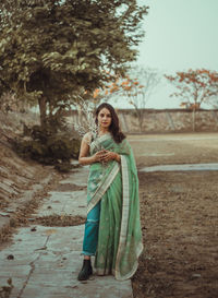 Portrait of young woman standing against tree