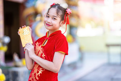 Portrait of smiling woman holding red while standing outdoors