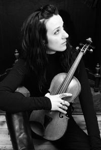 Thoughtful woman holding violin while sitting on chair