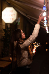 Side view of young woman pointing at illuminated light bulbs at night