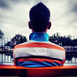 Rear view of boy sitting in city against sky