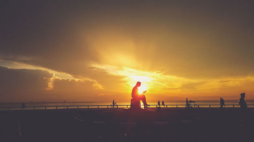 Silhouette people standing on beach against sky during sunset