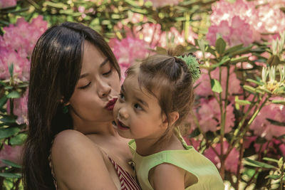 Woman kissing daughter while standing by plants