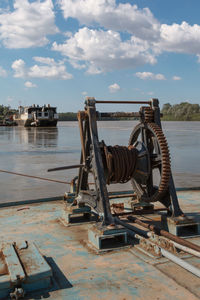 Old machinery on riverbank against sky