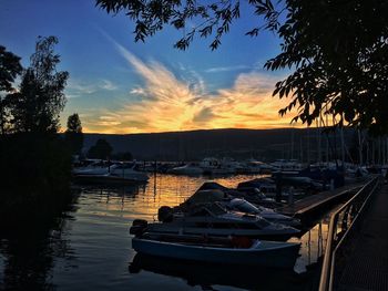 Boats moored on river in city against sky during sunset