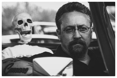 Portrait of mature man against skull in car during halloween