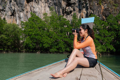 Young asian woman using camera to take photo while travel on long tail boat on summer vacation